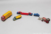 Full group shot of four metal vintage toy vehicles arranged left to right: a red and yellow truck, a green dump truck, a small blue truck, and a red tractor with front scoop.