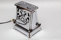 Image of the toaster from a left-side angle showing the Art Deco patterned chrome body and power cord.