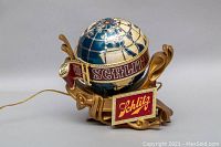 Full view of the illuminated Schlitz globe beer table lamp showing detail of the globe, Schlitz stickers, and gold decorative base.