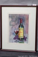 Full view of framed watercolour painting depicting a wine bottle, glass, and grapes.