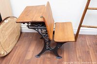 Side view of antique pine school desk showing foldable desktop and metal frame with ornate scrollwork.