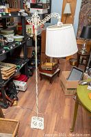 Full view of vintage white cast iron floor lamp with twisted shaft and fabric shade in a room with other items.