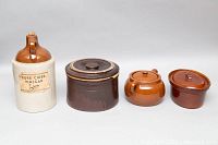 Full view of four vintage stoneware items: a tall Pure Cider Vinegar jug, large dark brown oval crock, two smaller brown crocks with lids.