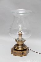 Full view of antique brass hurricane lamp showing glass chimney and brass base with electric cord.