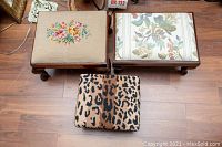 Top view of three footstools: one with needlepoint floral cushion, one with floral upholstery, and one smaller leopard print cushion.