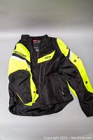 Full front and side view of the black and neon yellow Teknic motorcycle jacket, showing shape, color block design, and sleeve buttons.