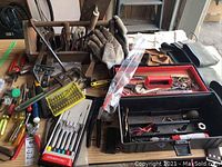 Wide view showing a wooden tool box with various hand tools such as hammers, screwdrivers, pliers, work gloves, and tool boxes.