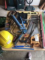 View of entire tool lot on table showing hard hat, grease gun, saws, clamps, and levels.