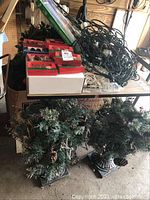 Photo of table with multiple boxes and tangled string lights on top, two green pine wreaths and decorative urns placed underneath table.