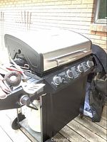 Char-Broil propane barbecue grill with control knobs, side burner, and utensils on top.