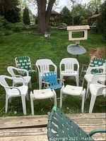 Front view of six white resin chairs and two vintage green webbed folding chairs plus one blue child-size webbed folding chair set outdoors on grass.