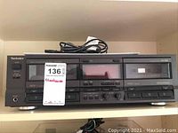 Front view of the Technics RS-TR355 stereo double cassette deck showing both cassette compartments, buttons, and included power cord on top.