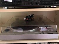 Overall view of Hitachi HT-21 turntable with clear dust cover in place and RCA cables coiled on top