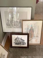 Three framed pen and ink architectural drawings shown leaning against a wall and floor. Illustrate three different Canadian buildings including the Victoria Hotel, Gooderham Building, and Parkdale Collegiate.