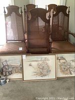 Group shot of three framed watercolour paintings leaning against chair background.