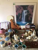 Overview of the collection showing ceramic canisters, mugs, wooden animal carving, framed waterfall print, small decorative items, clock, salt and pepper shakers, faux plant, and books on the floor.