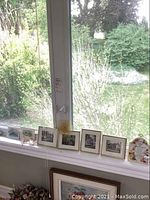 Image of four small framed prints of houses and additional decorative items on a windowsill including a sun catcher and a wood carved house.