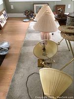 View of two pink ceramic base table lamps with light beige pleated cloth shades and two brass-colored wall-mount lamps with articulating arms on carpeted floor