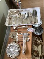 Overview of flatware set arranged on table including forks, knives, spoons, serving utensils, and butter dish.