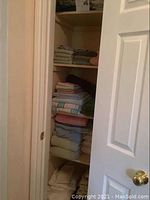 Shelf with stacks of folded sheets and linens including flannel and cotton sheets for double beds, and towels