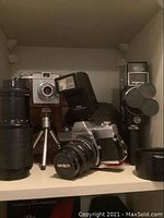 Minolta SR-T 200 camera with lens, Vivitar flash unit, Kodak POM 135 camera, Fujica 8mm movie camera, and tripod on shelf