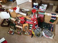 Photo showing multiple Christmas decoration boxes and loose items including ornaments, stockings, lights, and garlands on carpet