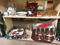 View of upper and lower shelves with teaset, serving platters, glass mugs, glasses, faux floral arrangement, and candle