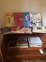Full view of music books and sheets arranged on a wooden desk, showing various titles and colorful covers.