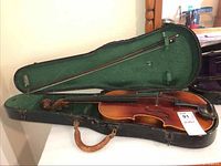 Full violin in open hard case with bow inside. The violin is reddish brown with black fingerboard and chinrest, case has green padded interior.