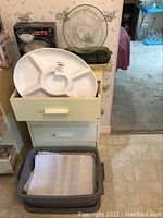 Open drawer with a white ceramic sectioned serving tray and stack of fabric placemats beneath.