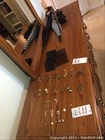 Wide view of issued lot showing cufflink sets laid out on wood table, two wallets, and four umbrellas on/behind the table.