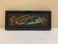 Front view of the framed abstract artwork showing colorful shapes on dark background.