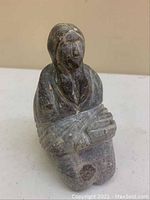 Front view of Native lady stone sculpture showing carved facial features and wrapped shawl.