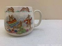 Full side view of ceramic Bunnykins mug illustrating a detailed knitting scene with running rabbits along the top band.