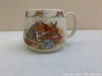 Photo of a ceramic Bunnykins mug with detailed illustrations of rabbits around a house scene.