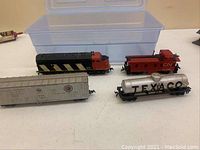 Photo showing four model train cars: black and red CN locomotive, red caboose, gray boxcar, and white TEXACO tanker car.