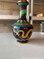 Front and side view of the Asian cloisonné vase showing the detailed dragon design, black crackled background, and decorative motifs on the neck and base. Visible dents present as noted by the seller.
