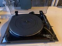 Front angled view of Ion Profile LP USB turntable showing platter, tonearm, and branding on glossy black base.