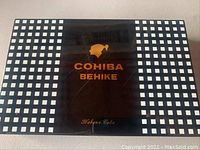 Top view of the Cohiba Behike cigar box showing the black and white checkered pattern with central gold logo and text.
