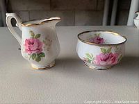 Side view of creamer and sugar bowl side by side showing pink rose floral designs and gold trim