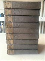 Photo showing side view of 9 books stacked horizontally with embossed designs and gold text on spines.