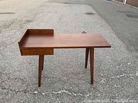 Front view of walnut desk showing raised back panel, drawer housing, and tapered legs.