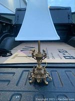 Front view of the Italian brass table lamp showing the detailed ornate brass base, brass stem, and white fabric lampshade.