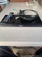 Photo of LG Blu-ray player on a beige table, showing remote control and HDMI cable placed on top.