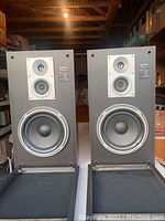 Pair of Technics speakers with front fabric covers removed, showing three drivers each: tweeter, midrange, and woofer. The speakers appear to be black with silver driver rims.
