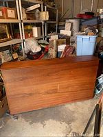 Full view of the teak headboard showing wood grain and storage base in a cluttered garage environment.