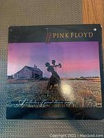 Photo of Pink Floyd vinyl record with cover featuring a person holding a trumpet in a field at sunset with a rustic house in the background.