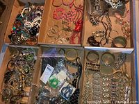 Overview of multiple boxes containing assorted costume jewelry pieces including bracelets, necklaces, and earrings.