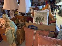 View of large ceramic Mary statue with chipping paint next to boxes holding religious figurines and throw pillows.