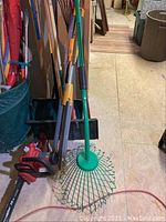 Side view showing electric Homelite chainsaw with red body and blade guard, and various garden and snow tools stacked behind.